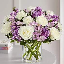 White roses and purple flowers arranged in a clear glass vase