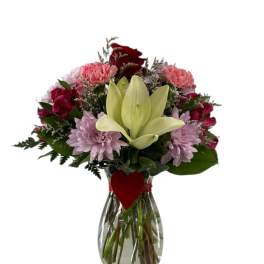 Bouquet of mixed pink and red flowers in a glass vase with a heart tag