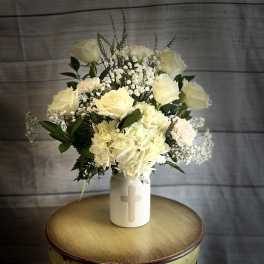 Cream roses and hydrangeas in a white vase with a cross