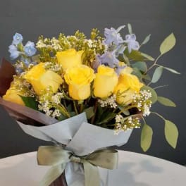 Yellow roses with small blue flowers in a wrapped bouquet