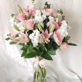 Pink lilies and roses arranged in a clear glass vase with white filler flowers.