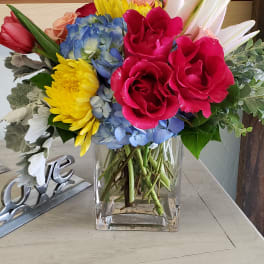 Colorful bouquet in a clear glass vase with roses, tulips, hydrangea, and daisies