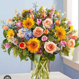 Mixed bouquet of sunflowers, roses, and tulips in a glass vase