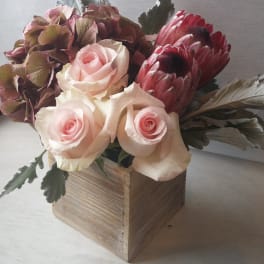 Pink roses and burgundy protea in a wooden box arrangement