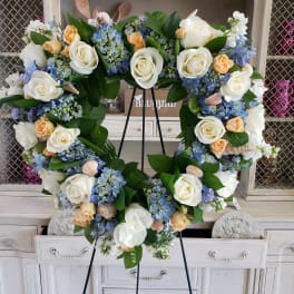 Heart-shaped floral wreath with white roses and blue hydrangeas on a stand