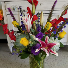 Mixed bouquet of lilies, roses, and purple flowers in a glass vase