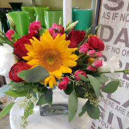Bouquet with a sunflower, red roses, and pink blooms in a glass vase