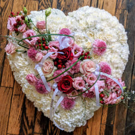 Heart-shaped white floral tribute with pink and red flowers and white name ribbons