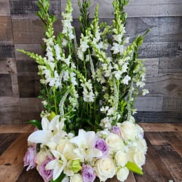 Tall white snapdragons with white lilies and ivory and lavender roses in a structured front-facing arrangement.