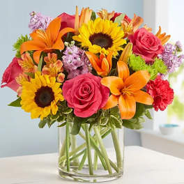 Bright mixed bouquet in a clear glass vase with sunflowers, roses, lilies, and carnations