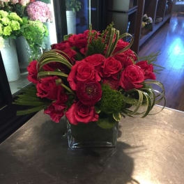 Red rose arrangement in a square glass vase with curled greenery
