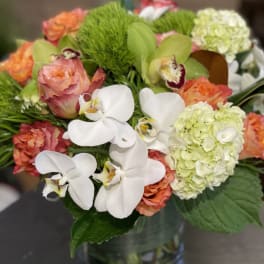 Bouquet of white orchids, peach roses, and pale hydrangeas in a glass vase
