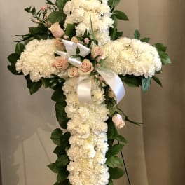 White floral cross on an easel with pink roses and ribbon