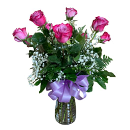 Medium vase arrangement of pink roses with white filler flowers and a lavender ribbon bow