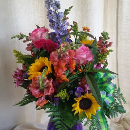 Mixed bouquet in a purple vase with sunflowers, roses, and purple spikes