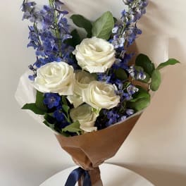 Bouquet of white roses and blue delphinium wrapped in brown paper