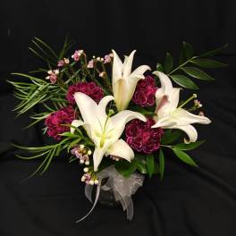 White lilies and magenta carnations in a glass vase with ribbon