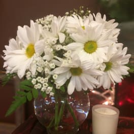 White daisy bouquet in a glass vase with a small candle beside it