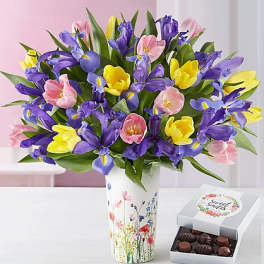 Bouquet of purple, pink, and yellow tulips in a floral vase beside a box of chocolates