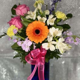 Mixed bouquet with pink roses, orange gerbera daisy, and white flowers in a blue vase