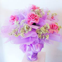 Pink roses with white baby's breath in a purple-wrapped bouquet