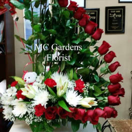 Tall arrangement of red roses and white lilies with a teddy bear
