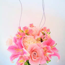 Pink lilies and a rose in a glass vase with hanging silver cords