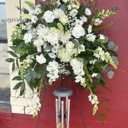 Large white funeral spray on a black easel with wind chimes below