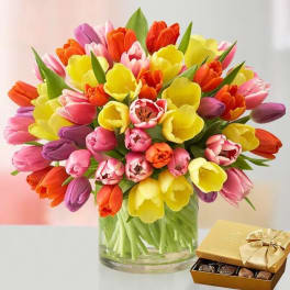 Colorful tulip bouquet in a glass vase beside a box of chocolates