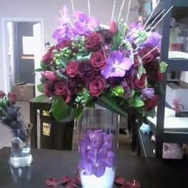 Purple and burgundy floral arrangement in a clear vase with a purple orchid cylinder centerpiece