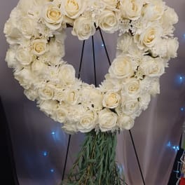 Heart-shaped white floral wreath on a stand with trailing greenery