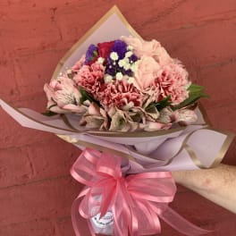 Pink and purple mixed bouquet wrapped in paper with a pink ribbon