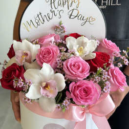 Pink and red roses with white orchids in a round box for Mother’s Day