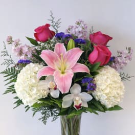 Bouquet of pink roses, lilies, hydrangeas, and orchids in a glass vase