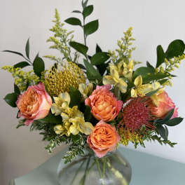 Bouquet of peach roses and yellow flowers in a round glass vase