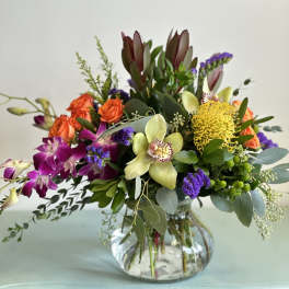Mixed bouquet in a clear glass vase with orchids, roses, and yellow pincushion blooms