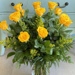 Yellow roses arranged in a clear glass vase with greenery