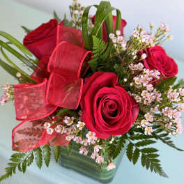 Red roses with pink filler flowers and a red ribbon in a glass vase