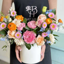 Mixed bouquet of pink, peach, orange, and blue flowers in a white box
