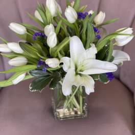 White tulips and a white lily in a glass vase with purple filler flowers
