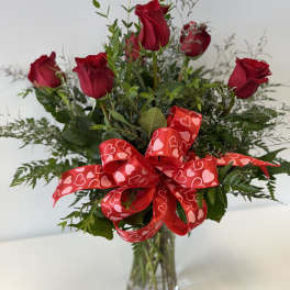 Red roses in a clear glass vase with a heart-patterned ribbon