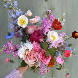 Handheld bouquet of pink, blue, and white mixed flowers