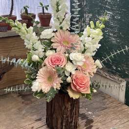 Pink roses and gerbera daisies in a rustic wood vase with white snapdragons