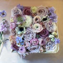 Box of pastel roses and ranunculus with small purple flowers