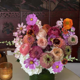Mixed bouquet of pink, purple, orange, and white flowers in a dark vase