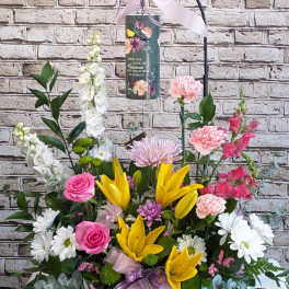 Standing floral tribute with lilies, roses, and daisies around a memorial plaque