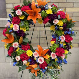 Colorful floral wreath on a black stand with orange lilies and pink roses