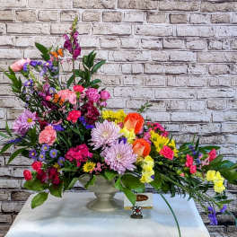Colorful mixed flower arrangement in a pedestal vase with butterfly accents