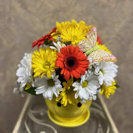 Colorful daisy bouquet in a yellow smiley-face pot with a decorative butterfly