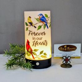 Lit memorial candle with birds and the words Forever in our Hearts